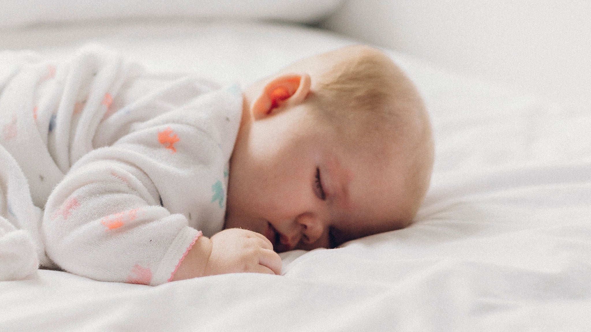 Baby in patterned onesie on white bed