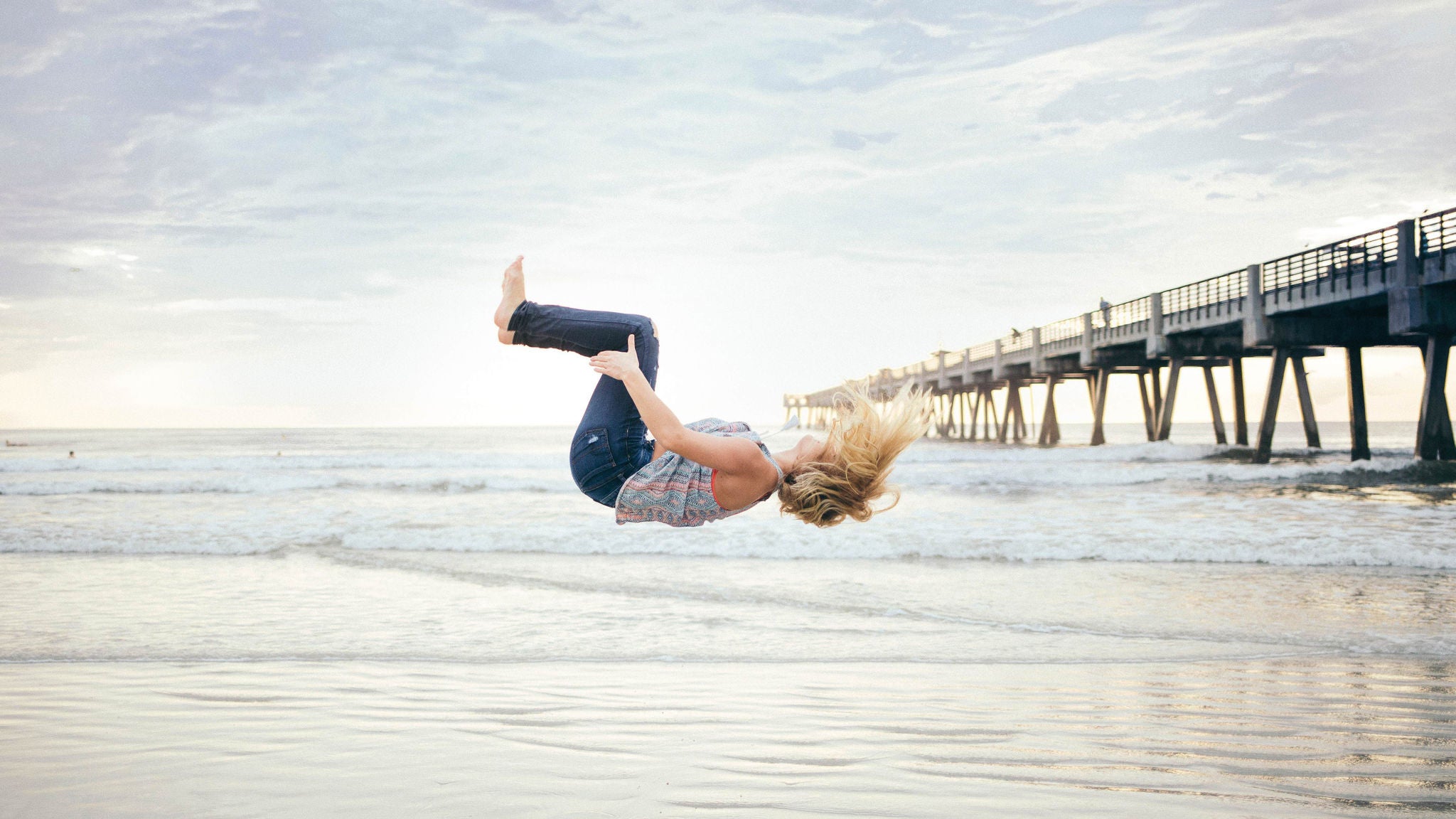 Woman flipping near ocean pier at sunset