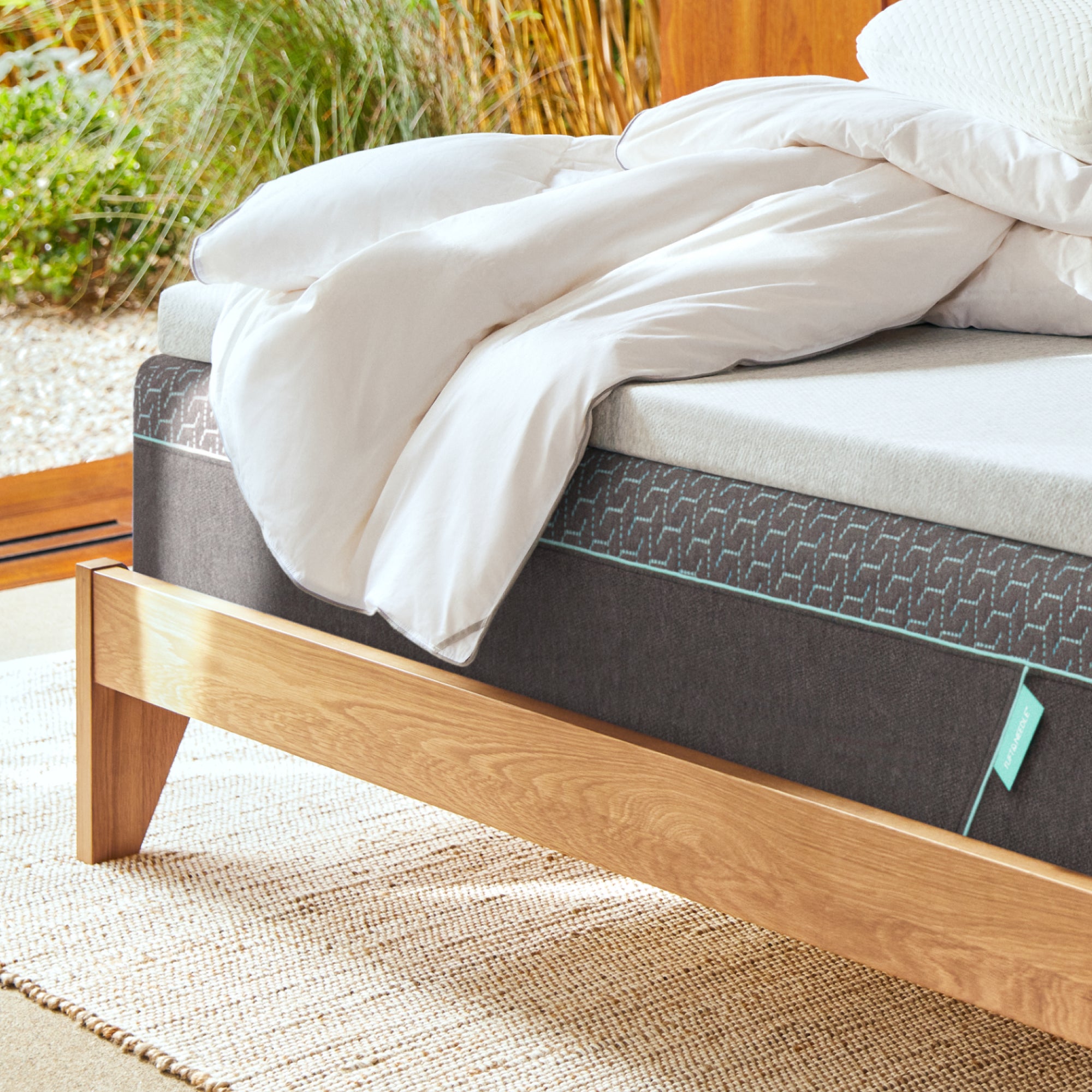 Tuft and Needle Mattress on a wooden bed frame with white down duvet insert on top with an outdoors background