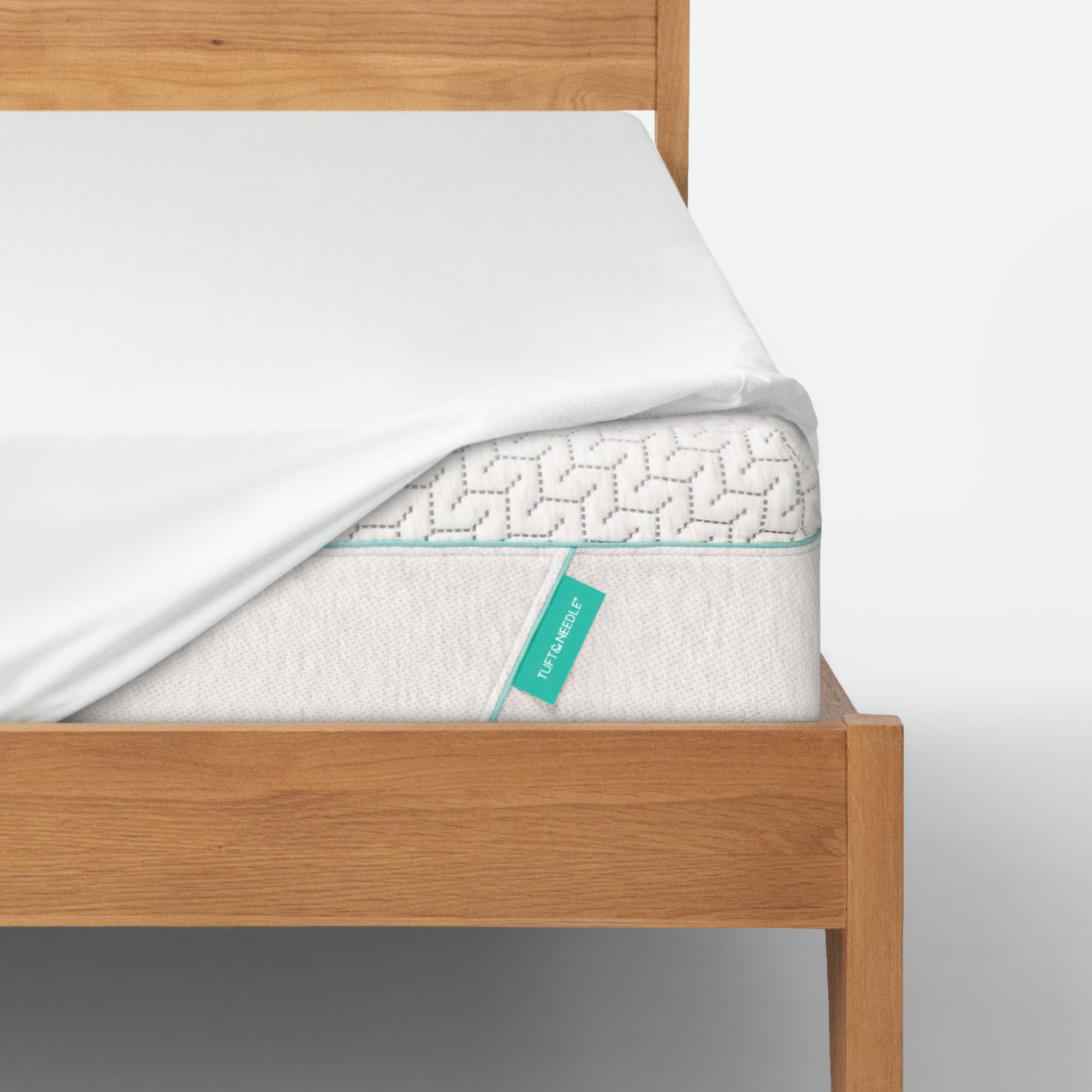 Tuft and Needle Mattress topper on a wooden bed frame with a visible brand label.