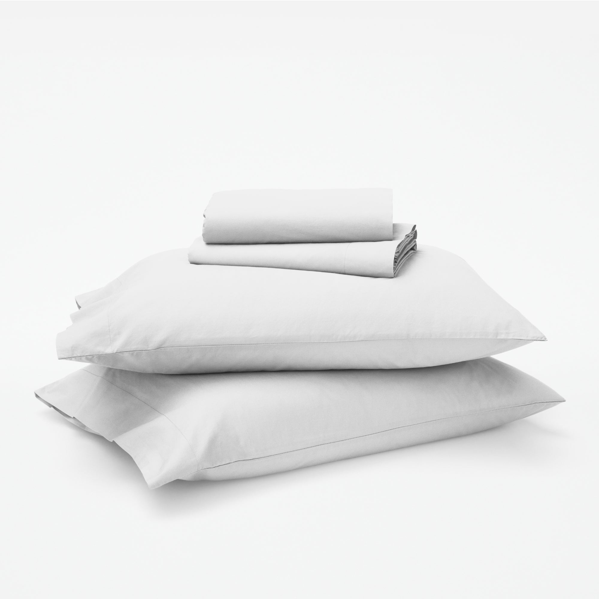 The Tuft and Needle Classic Percale Sheet Set, 1 sheet and pillowcases stacked on top of 2 pillows || color: Cloud